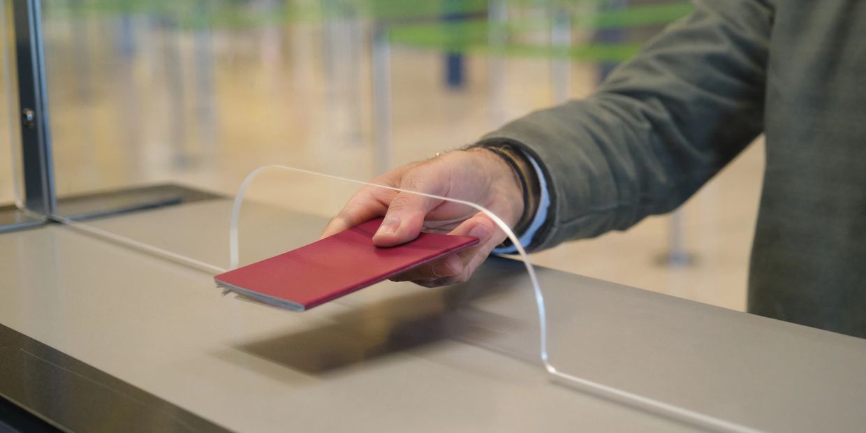 A person handing over a red passport at a counter with a protective screen.