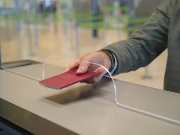 Mano entregando un pasaporte rojo en un mostrador.