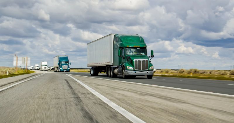 A green truck driving on Interstate 5 in California on an overcast day.