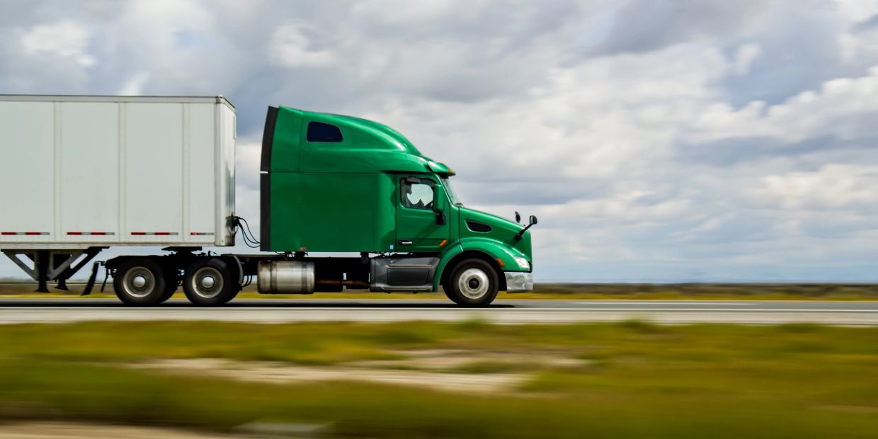 Green semi-truck driving on highway.