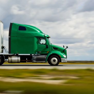 Green semi-truck driving on a highway.