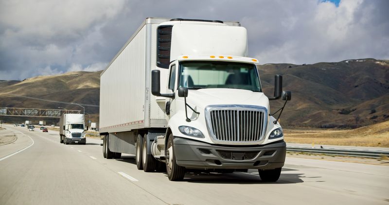 White cargo trucks driving on Interstate 5 in California on an overcast day.