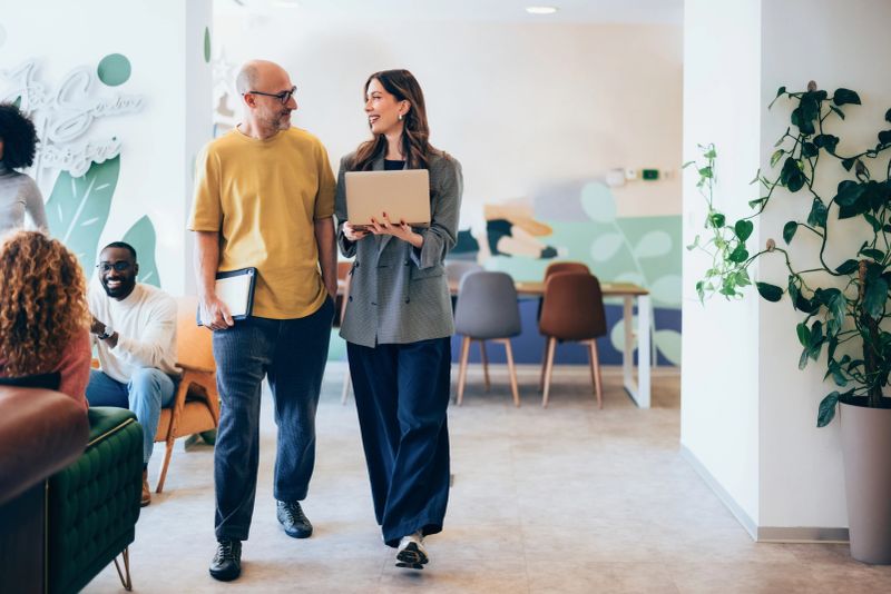 Colleagues in a contemporary workspace sharing ideas, with vibrant interiors and a relaxed atmosphere, showcasing collaboration and modern office culture.