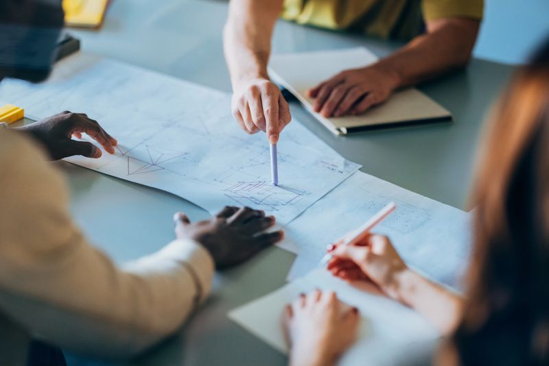 A small group of professionals collaborates on reviewing and discussing architectural blueprints during a design strategy session, focusing on innovation, teamwork, and effective planning in a modern workspace.