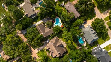 Aerial view of suburban homes with swimming pools and lush greenery.