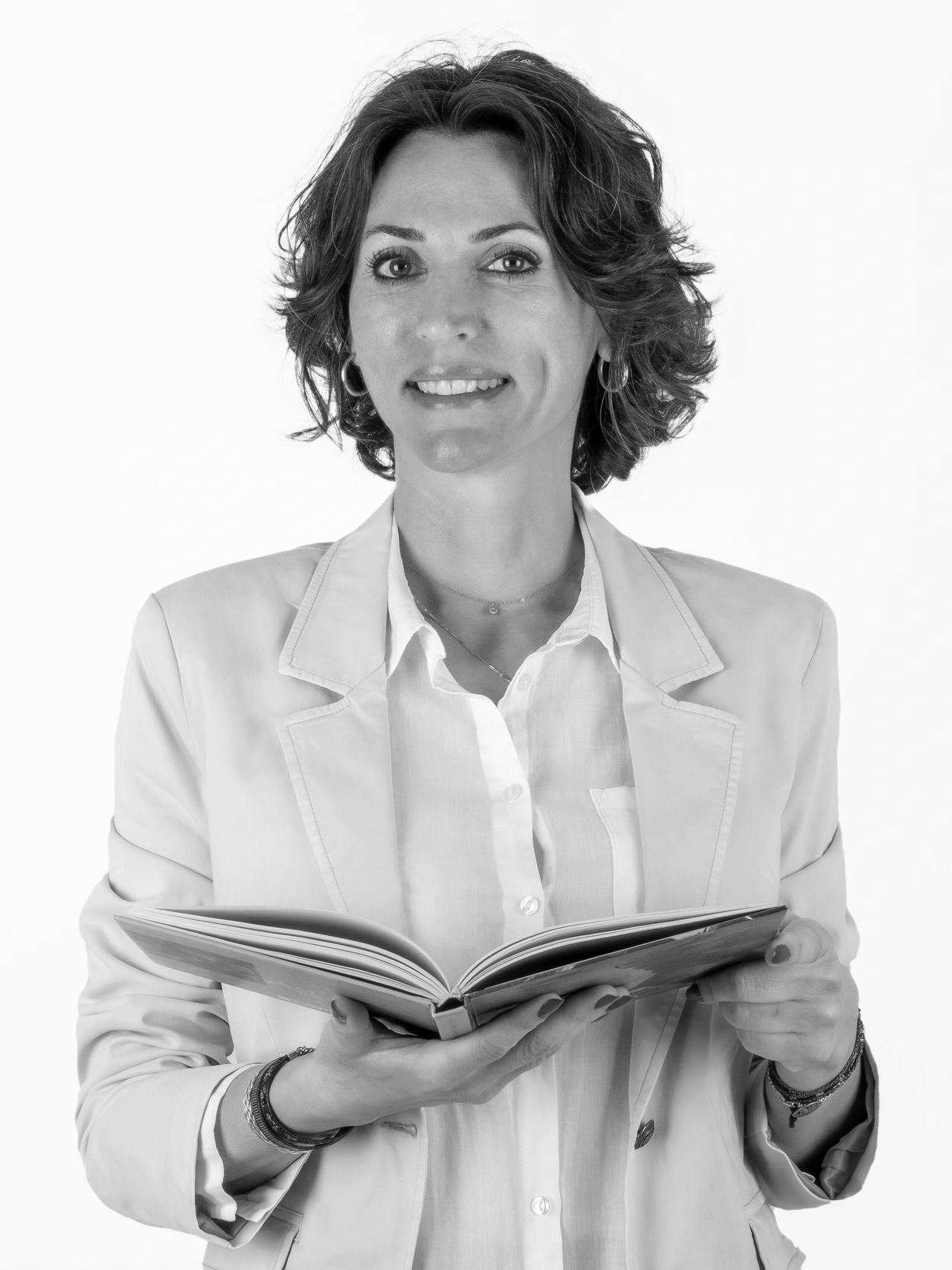 Woman in blazer holding an open book and smiling.