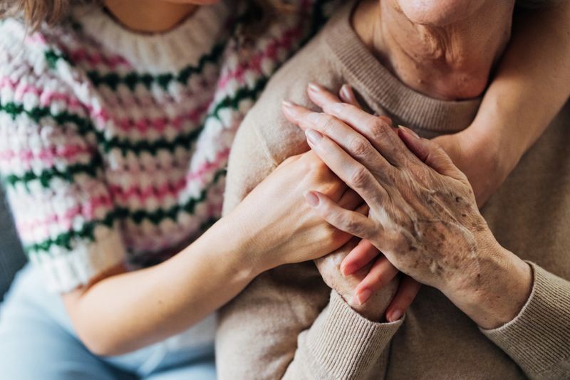 An elderly woman receives loving support as younger hands comfort her, portraying care and family connection.