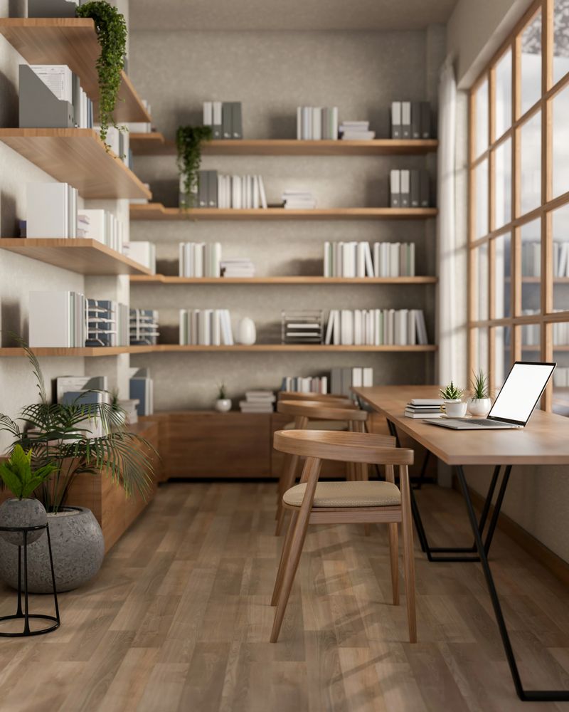 A white screen laptop on the long square table next to glass wall and large bookshelf. Cosy library or study room. 3D Rendering, 3D Illustration.