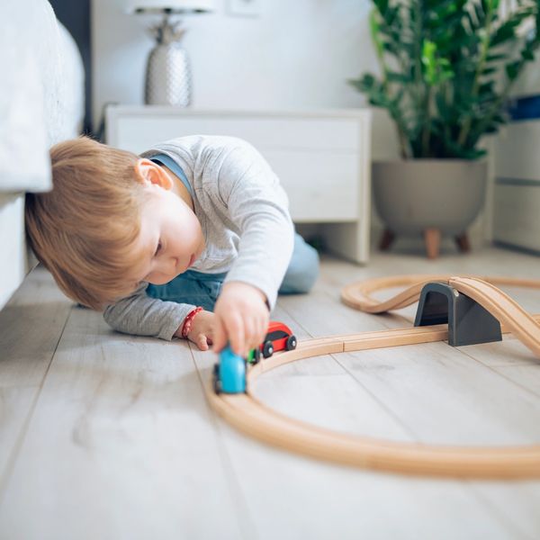 Young boy playing with a wooden train set on the floor.