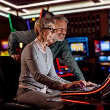A joyful older couple playing slot machines in a casino.