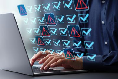 Person typing on laptop with digital warning and checkmark icons overlay.