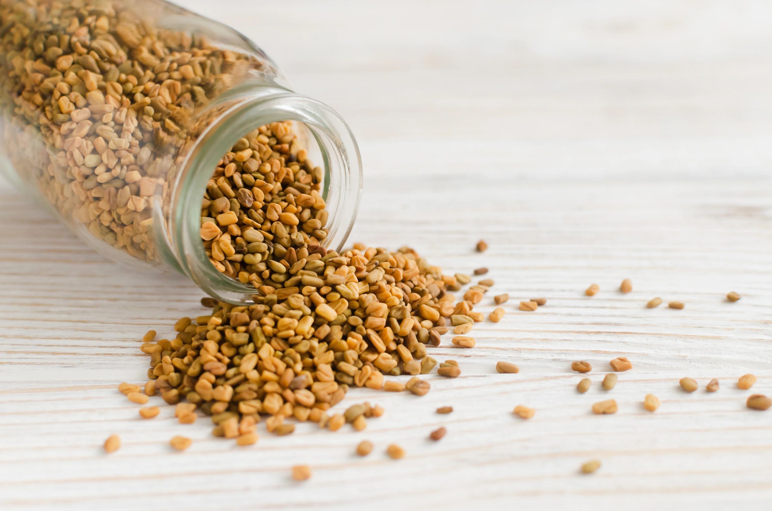 Glass jar spilling seeds on a light wooden surface.