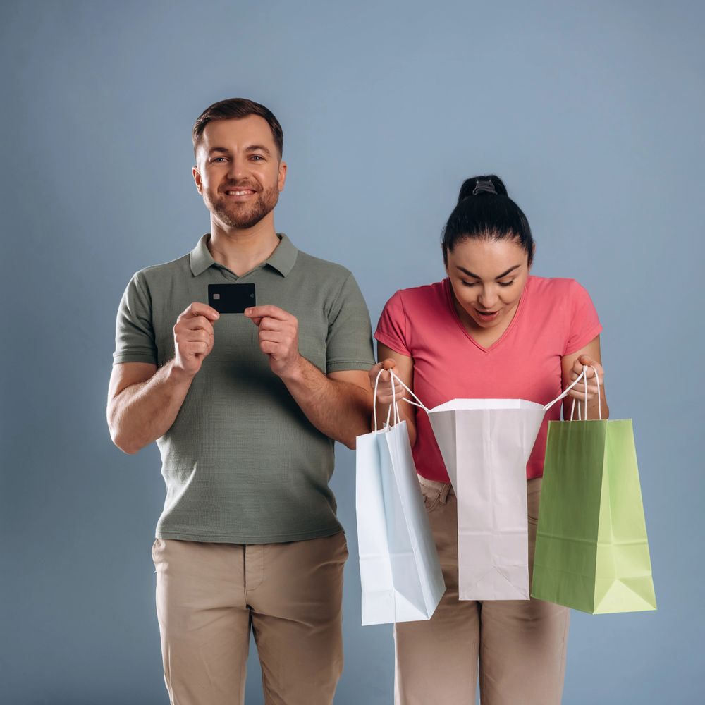 Happy man holding credit card and woman excitedly looking into shopping bags.