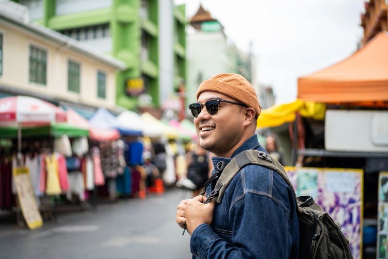 Young Asian traveling backpacker in Khaosan Road outdoor market in Bangkok Thailand. Happy tourist walking in the downtown street traditional market