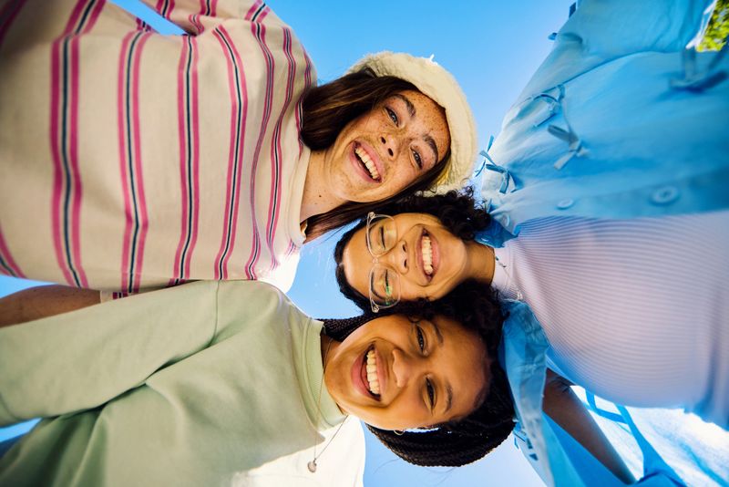Three Gen Z girls embracing and smiling at the sky