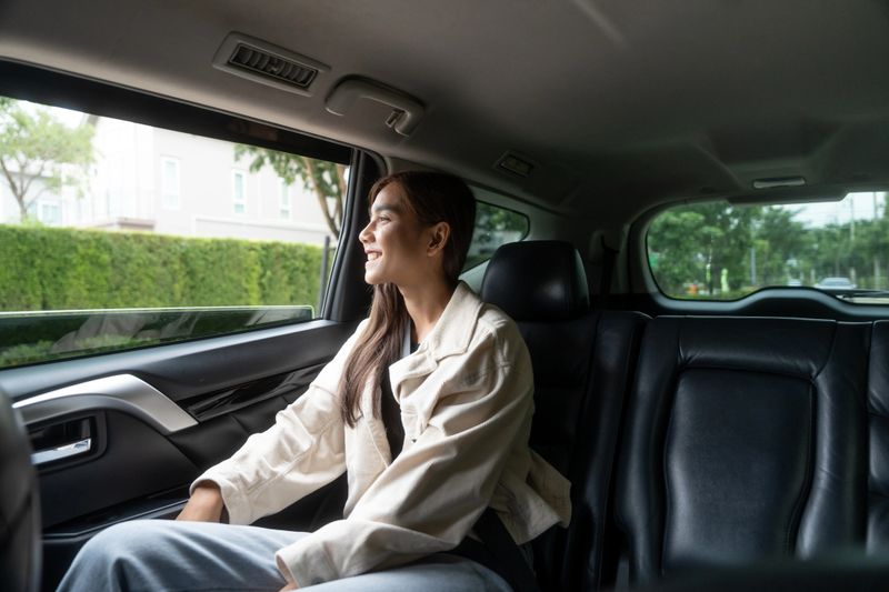 Relaxing moment of beautiful woman sitting in car back seats with safety belt and look out in the window. Female happy in car while traveling on the road to your destination.