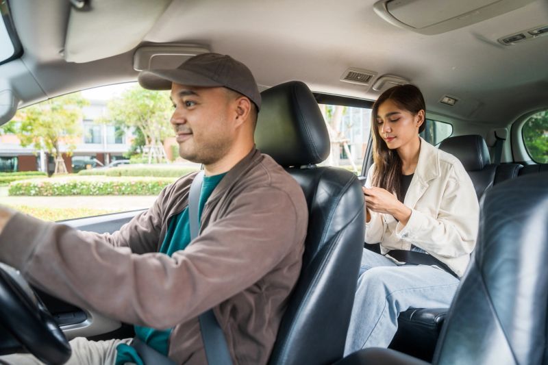 Young asian woman traveling in the downtown city with taxi driver service. Female passenger sitting in backseat calling taxi driver by application.