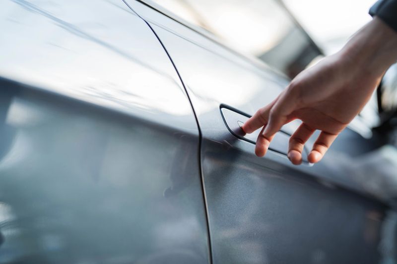 A close-up shot of a woman pressing the button on the door handle to unlock and open the door of her EV car before getting in the driver's seat