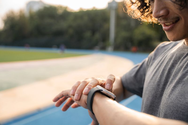 Close-up shot of athlete checking the fitness tracker app on his smart watch during training session, tapping on the screen monitor his performance, reviewing metrics like heart rate, pace, and distance