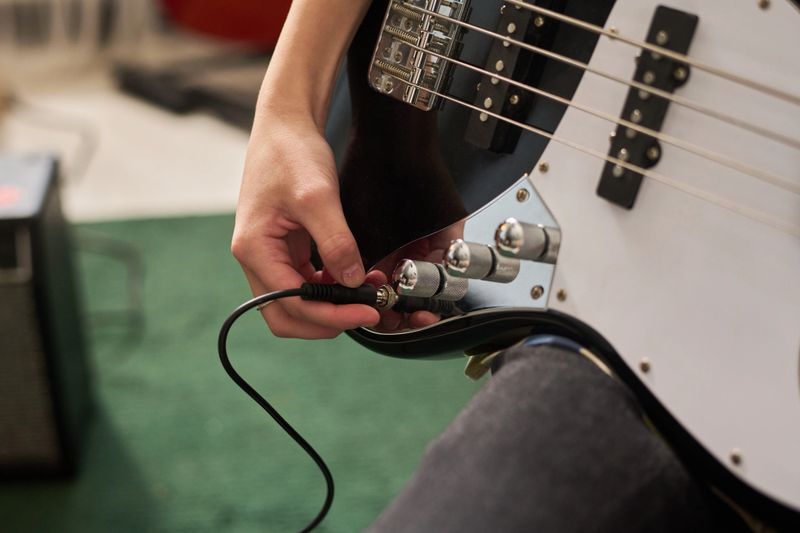 Close-up view of person adjusting volume and tone controls on electric guitar, focusing on hand interaction with instrument knobs in practice setting