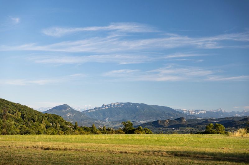 Picturesque La Dent Du Chat mountain landscape featuring rolling hills covered in lush green vegetation. The sky above is a brilliant blue, scattered with delicate, wispy clouds. This photo was taken near Grand Colombier famous summit in Bugey mountains, in Ain, Auvergne-Rhone-Alpes region in France with a bright beautiful sunset in august.