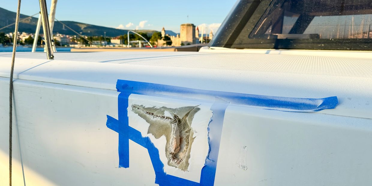Boat hull damage marked with blue tape for repair.