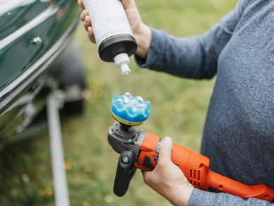 Person applying polish to a car buffer tool outdoors.
