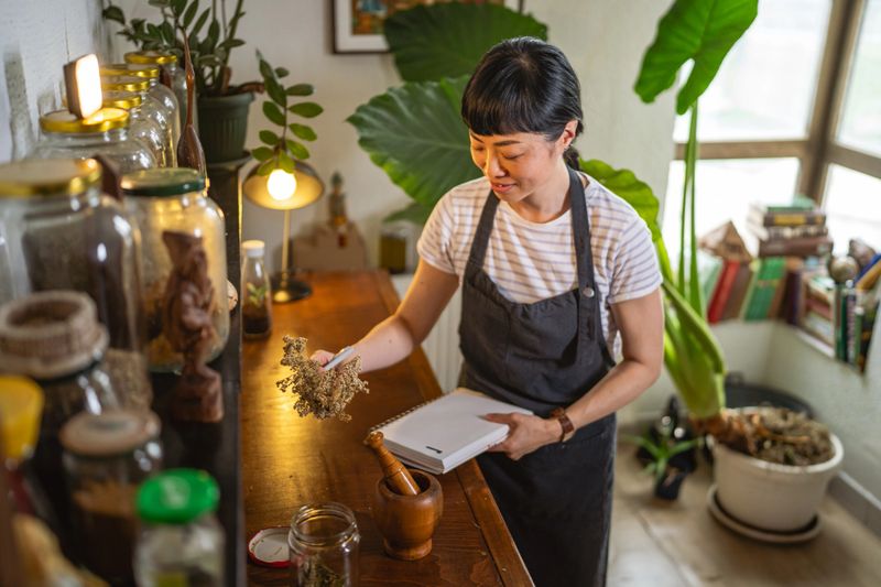 mature japanese woman wear apron and write recipes at notebook in herbal workshop