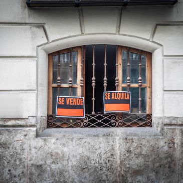 Window with 'For Sale' and 'For Rent' signs in Spanish.
