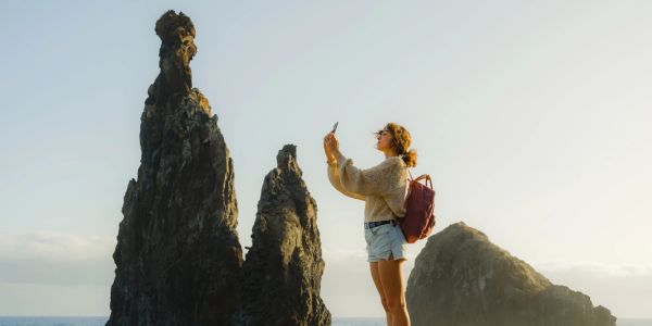 Woman photographing tall sea stacks at sunset.