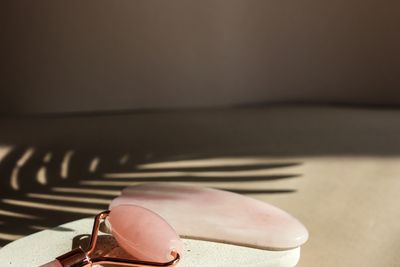 Rose quartz facial roller and gua sha stone on textured slabs with shadow.