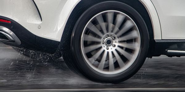 A cars wheel and tire moving at speed on a wet road.