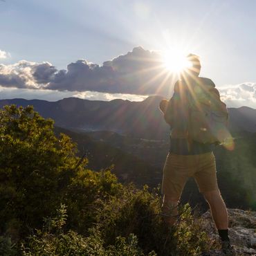 Person enjoying mountain view at sunset with sun flare.