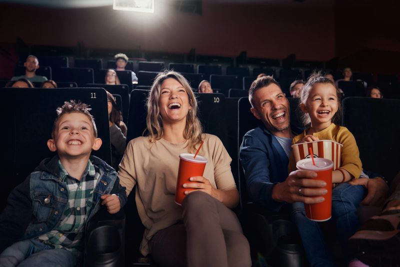 Cheerful parents and their kids having fun while watching a movie in theatre.