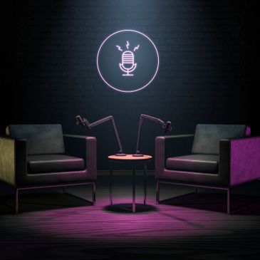 Two chairs and microphones under neon podcast sign.