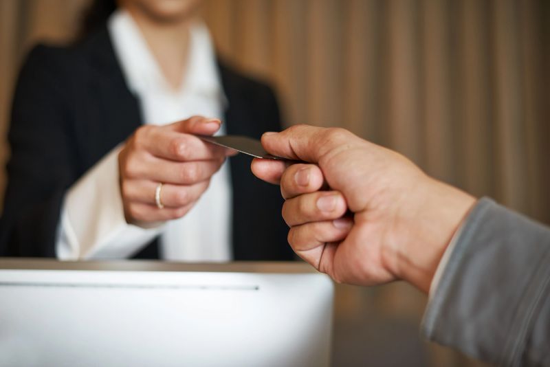 A hotel receptionist is handing a card to a guest, emphasizing professional service and hospitality. This scene highlights travel-oriented services, showcasing interaction between staff and clients in a modern hospitality environment.