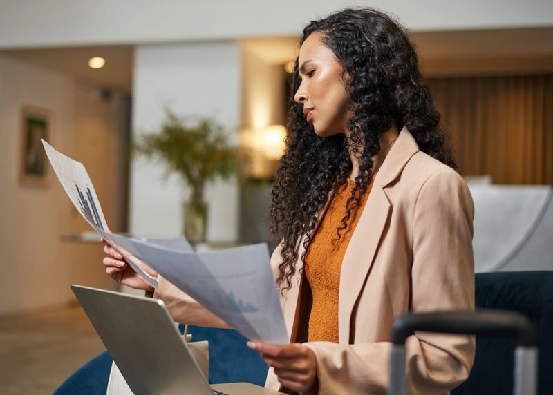 Focused young professional reviewing graphs and charts while using a laptop in a contemporary hotel lobby. The image showcases a business-oriented traveler working in a stylish and professional environment.