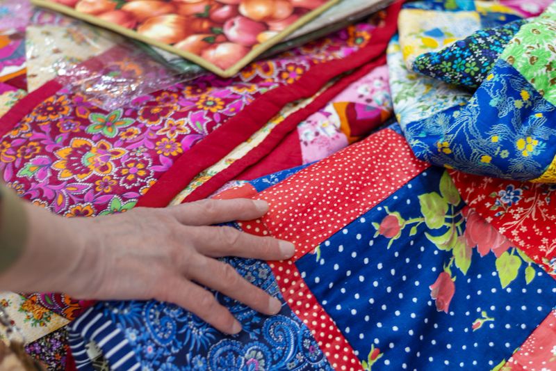 Hand gently touches bright patchwork quilt with lots of colorful floral and patterned fabrics. Buyer's Choice. Close-up.