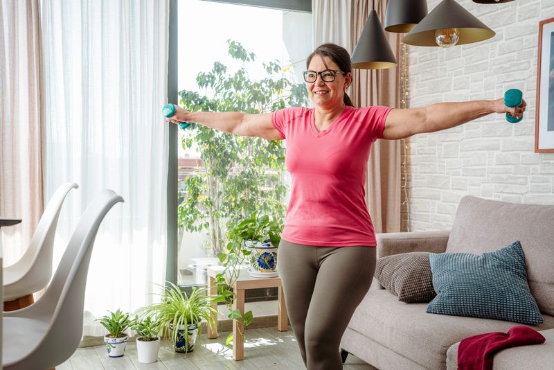 Mature overweight woman exercising with dummbells for her arms muscles. Muscular female working out with dumbbells