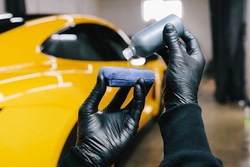 Process of pouring ceramic liquid from bottle on sponge to apply a protective nano layer on car. Detailing service worker applies ceramic protective liquid on sponge close-up
