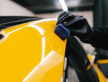 Hand polishing a yellow car's surface with a blue sponge.