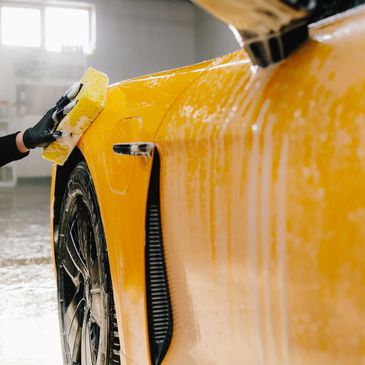 Person washing a yellow sports car with a sponge indoors.