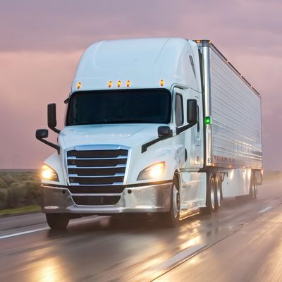 Two white semi-trucks driving on a wet highway during sunset.