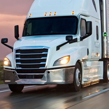 White semi-truck driving on wet road at sunset.