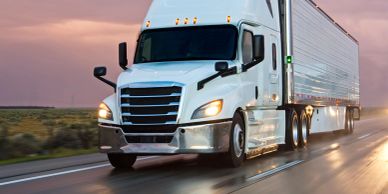 White semi-truck driving on highway during sunset.