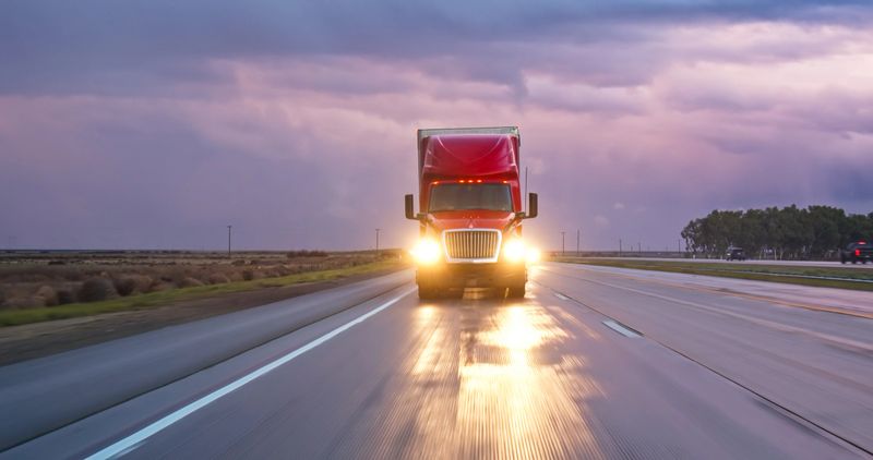 A semi-truck driving south on Interstate 5 in the Central Valley on a stormy evening.