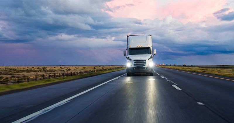 A semi-truck driving south on Interstate 5 in the Central Valley on a stormy evening.