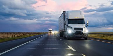 Semi-trucks driving on a wet highway at dusk.