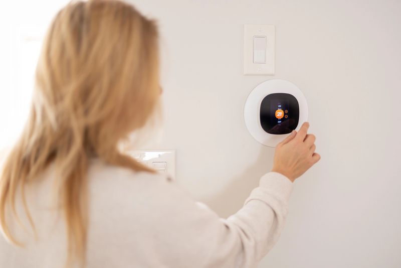 Finger interacting with a wall-mounted smart thermostat, adjusting settings to achieve a comfortable indoor temperature, showcasing modern technology and energy efficiency for home climate control.