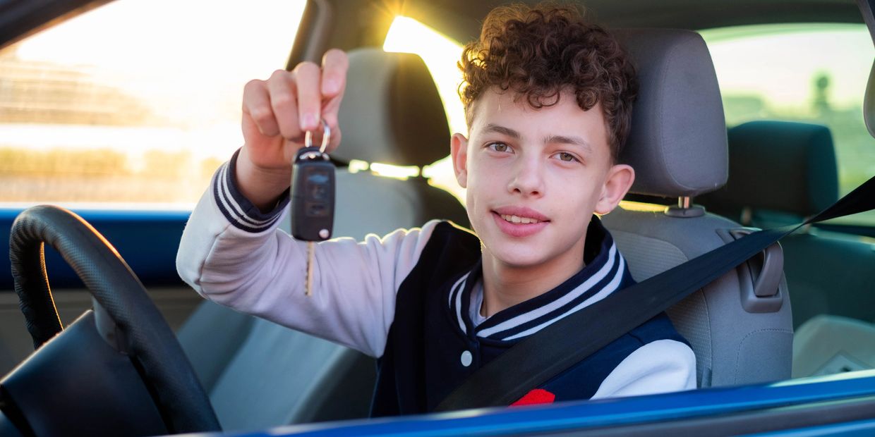 Teenager in the drivers seat, holding up a key fob.